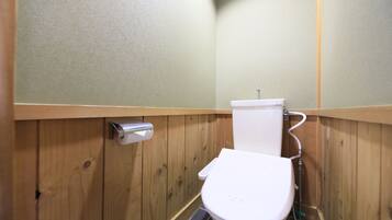 A small, wooden-paneled bathroom with a white toilet, a hand dryer, and a visible pipe.
