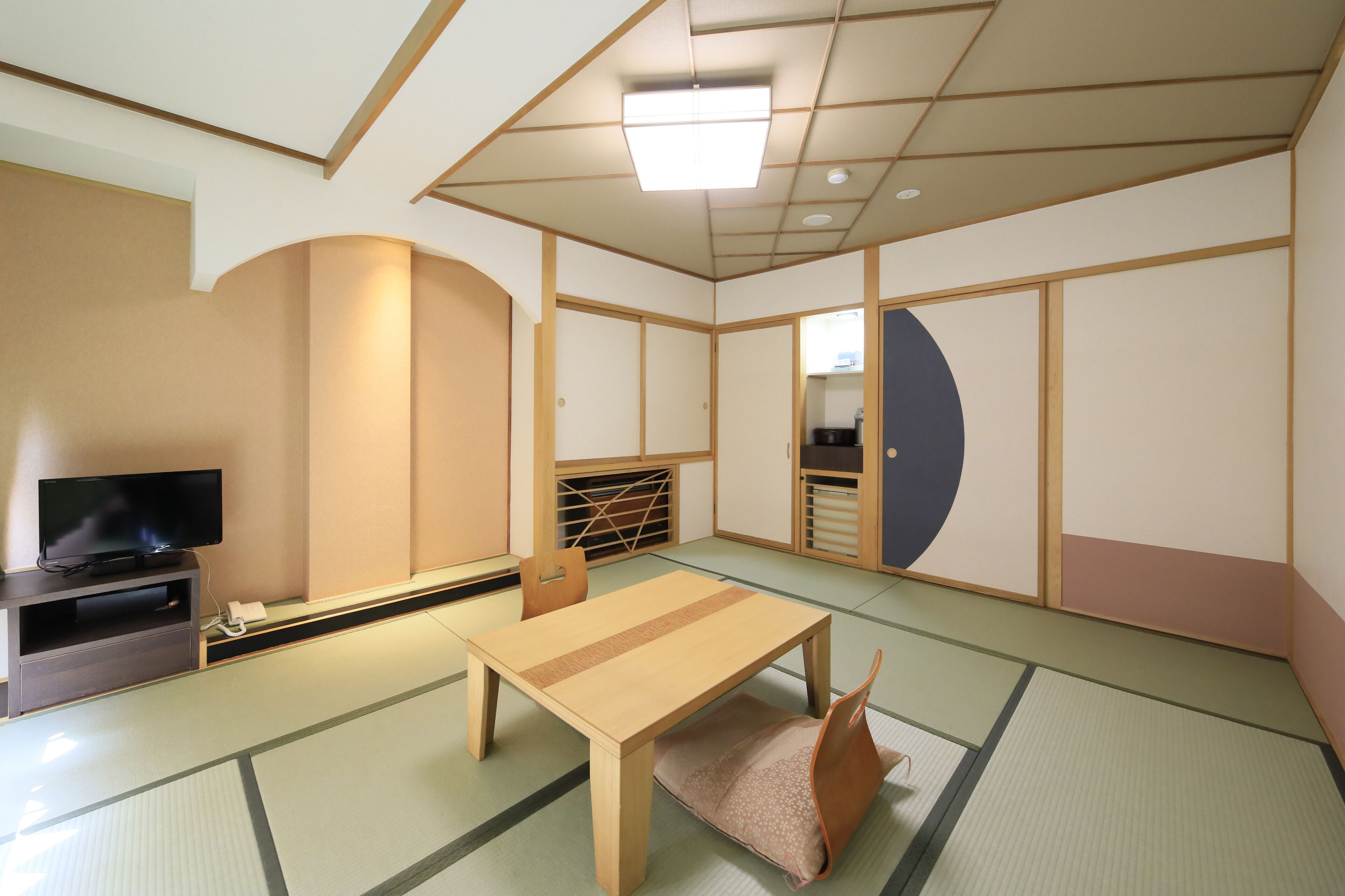 Una habitación japonesa tradicional con suelo de tatami, una mesa baja, un televisor y puertas correderas.