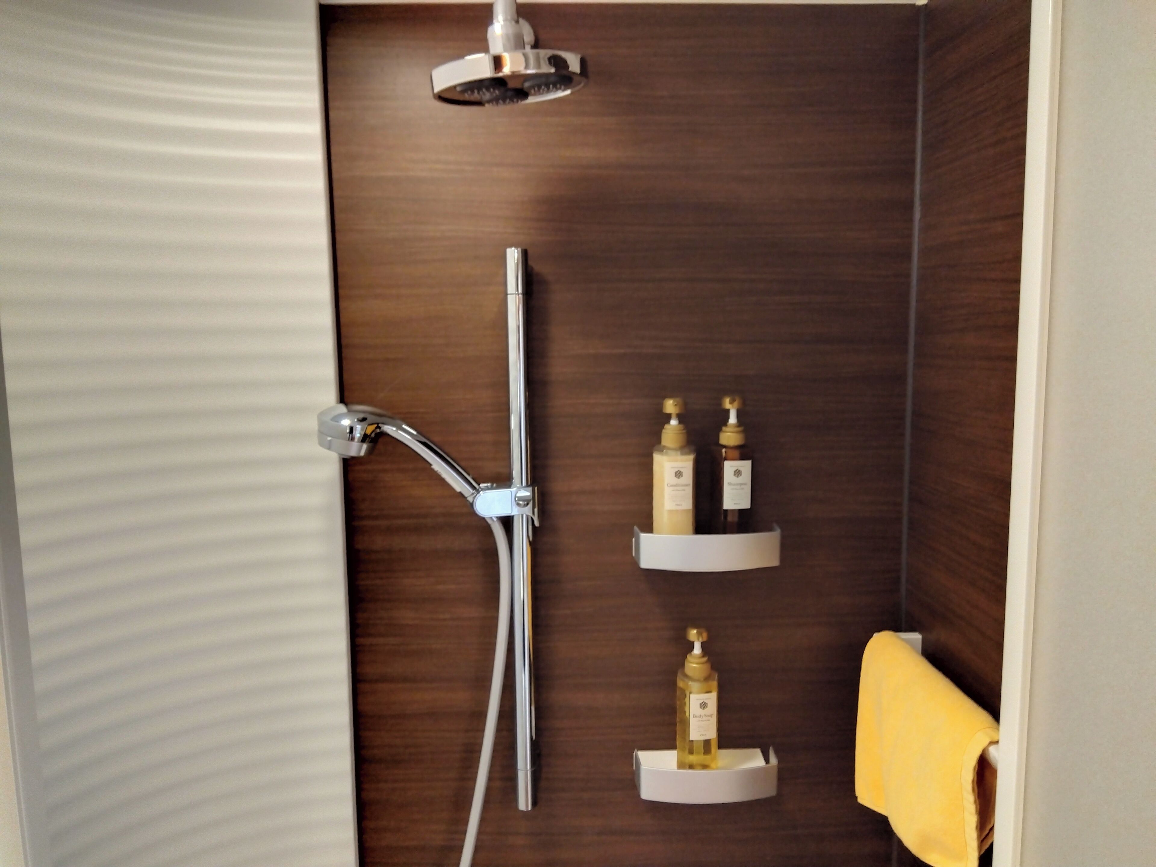 A shower area with a chrome showerhead and a handheld showerhead, two shelves with toiletries, and a yellow towel hanging on the wall.