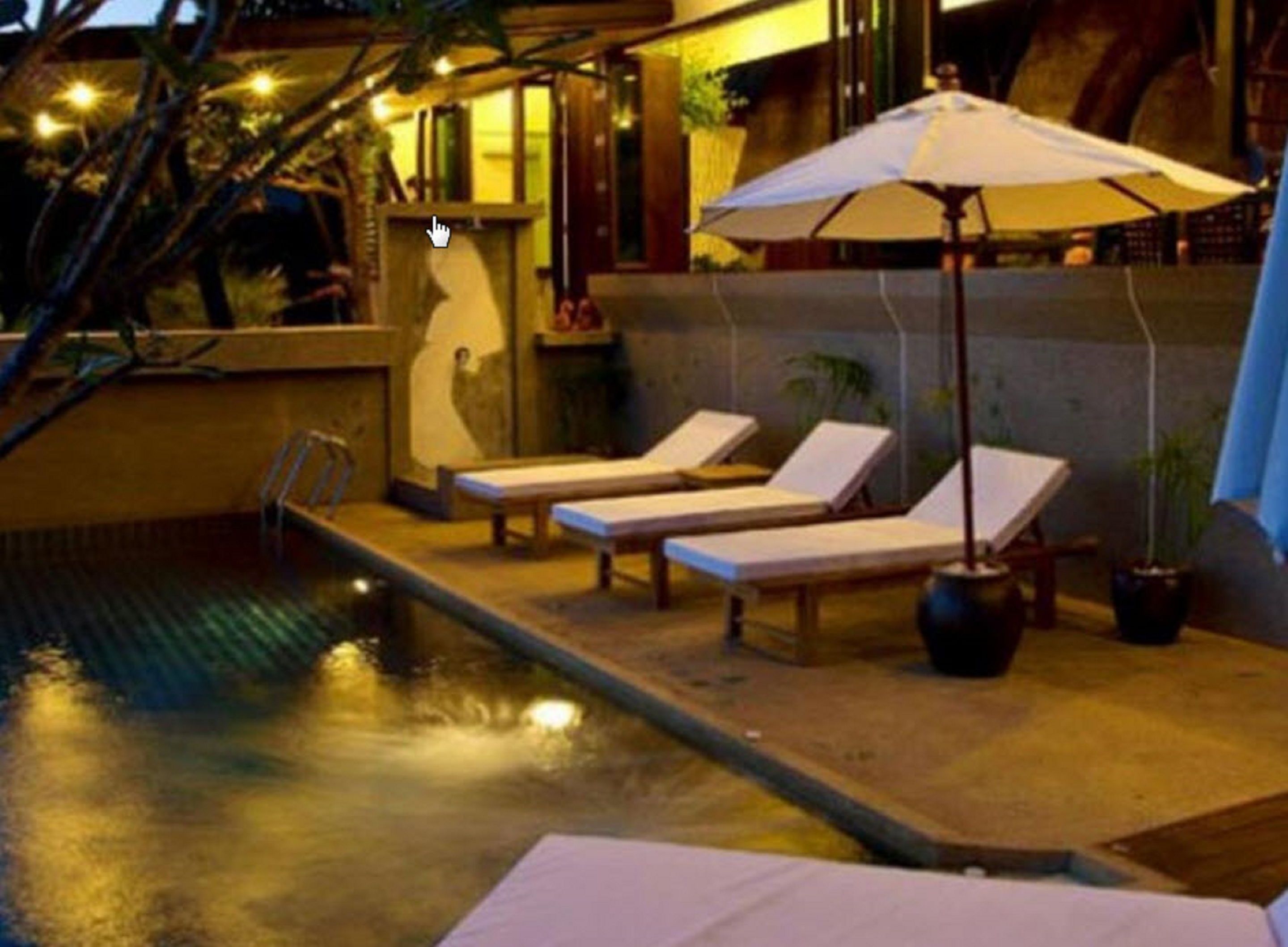 A poolside area with lounge chairs and a table, surrounded by potted plants and a glass enclosure.