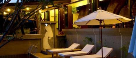 A poolside area with lounge chairs and a table, surrounded by potted plants and a glass enclosure.