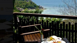 Terraza de madera con una mesa dispuesta para el desayuno, con vista al mar, vegetación y cielo despejado.