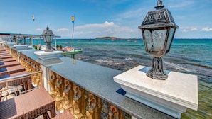 A seaside promenade with a stone balustrade, a white marble pedestal with a lantern, and a view of the ocean with boats. - Suntosa Resort (Koh Lan)