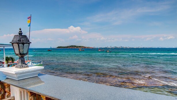 A waterfront view with a stone balustrade, a decorative lamp, and a flag. - Suntosa Resort (Koh Lan)