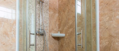 A glass-enclosed shower stall with a handheld showerhead and a wall-mounted faucet.