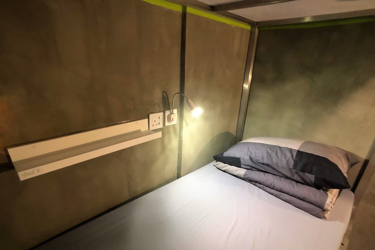 A single bed with a headboard, a bedside lamp, and a wall-mounted power outlet.