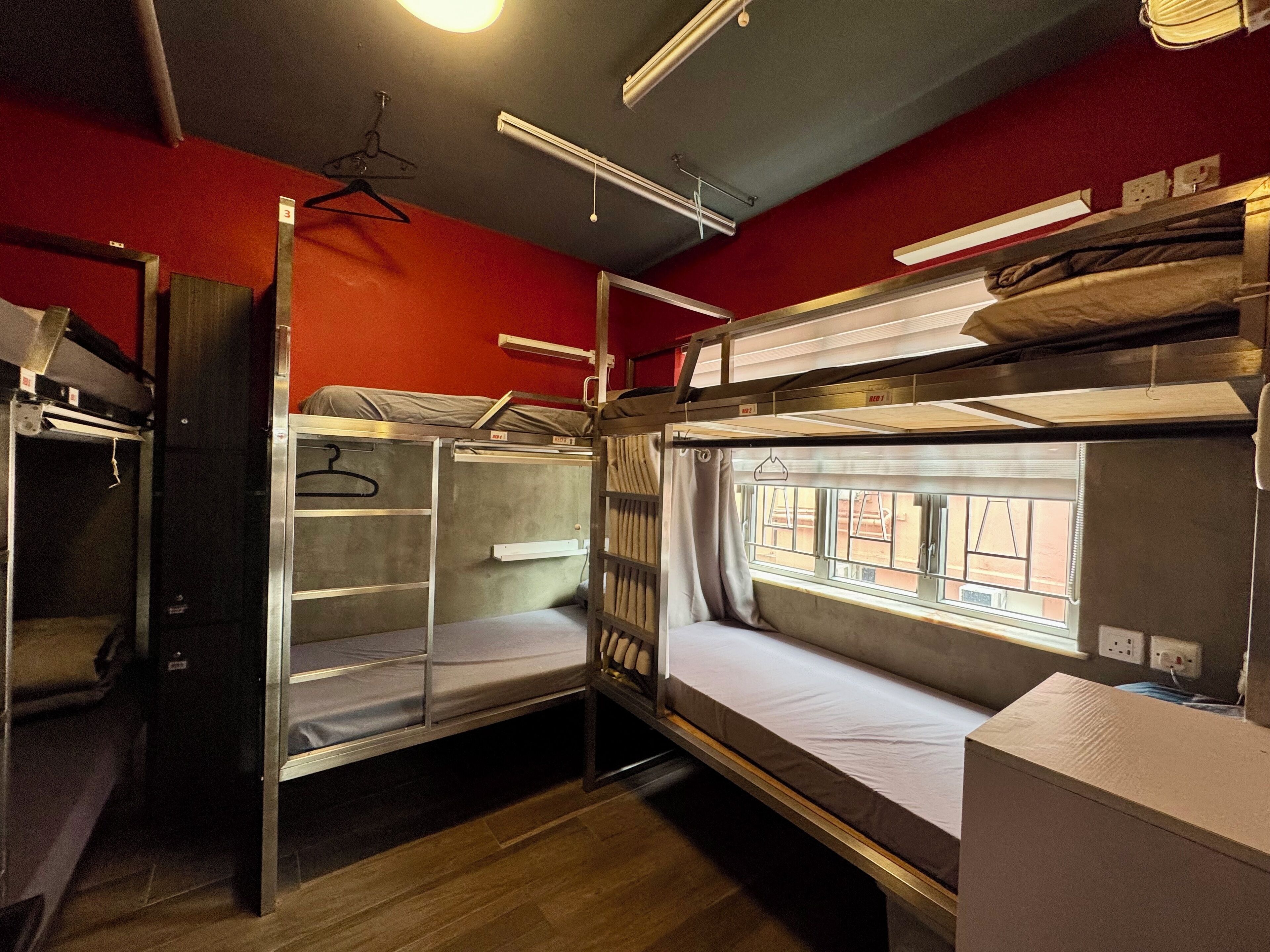 A bunk bed room with a window, a hanging coat rack, and a wooden floor.