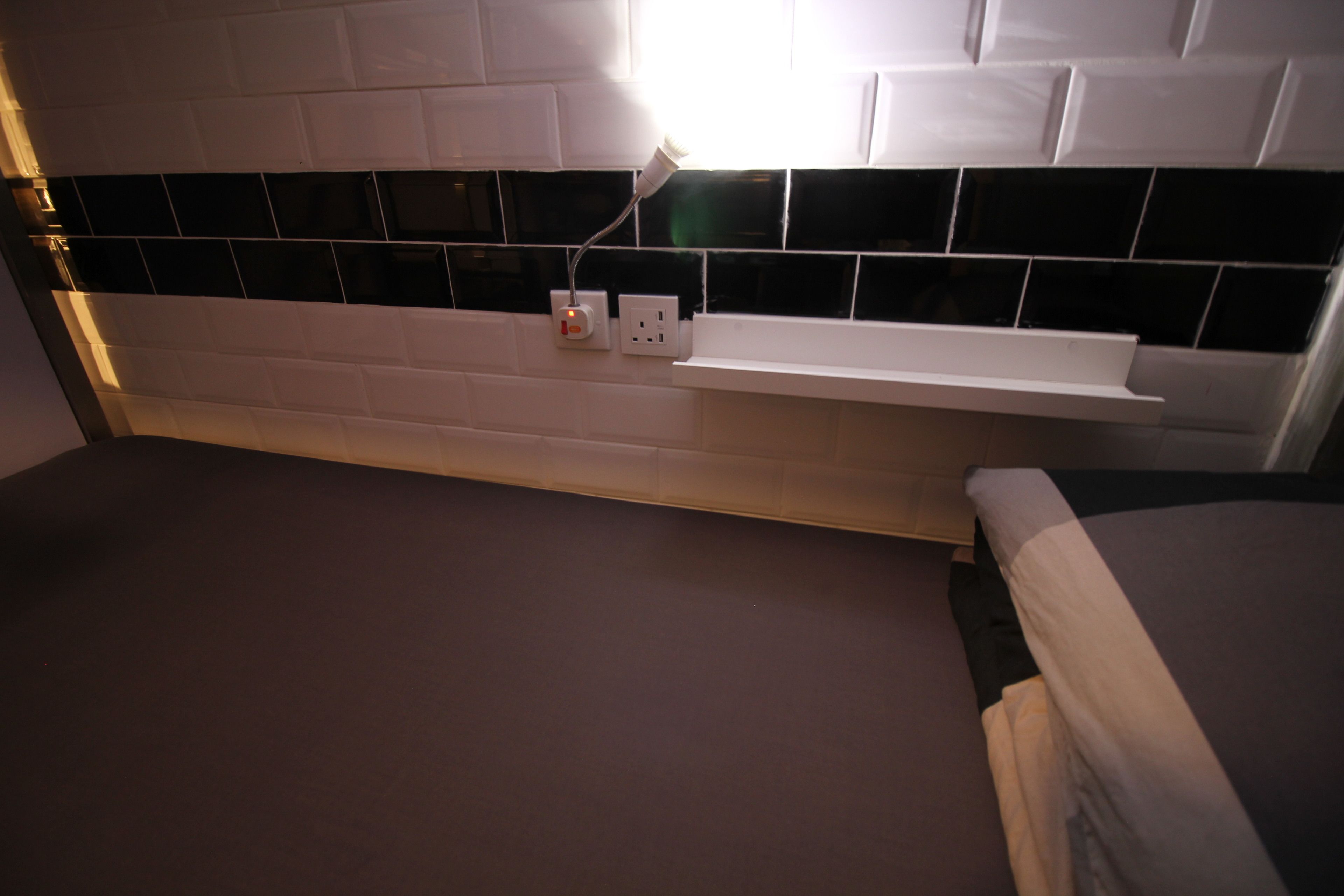 A bedroom with a white headboard, a bedside table, and a wall-mounted shelf.