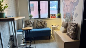 A cozy room with a blue sofa, a small round table, and a wall-mounted clock. - Urban Pack - Hostel (Kowloon)