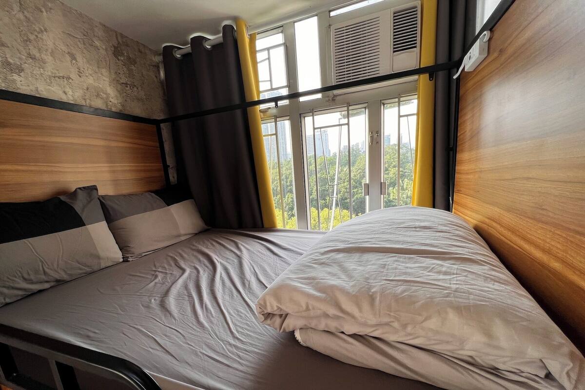 A bed with a wooden headboard, a window with curtains, and a view of greenery outside.