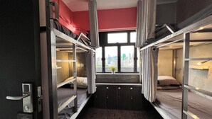 A bunk bed room with a city view through a window, a potted plant, and a door with a handle. - Urban Pack - Hostel (Kowloon)
