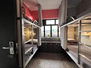 A bunk bed room with a city view through a window, a potted plant, and a door with a handle. - Urban Pack - Hostel (Kowloon)