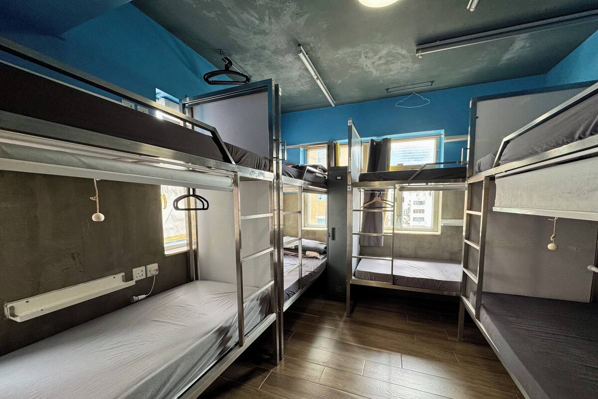 A dormitory room with bunk beds, a window with a view, and a hanging light fixture.