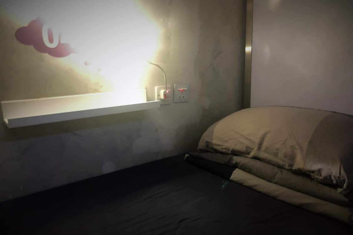 A dimly lit room with a bed, a wall-mounted light, and a power outlet.