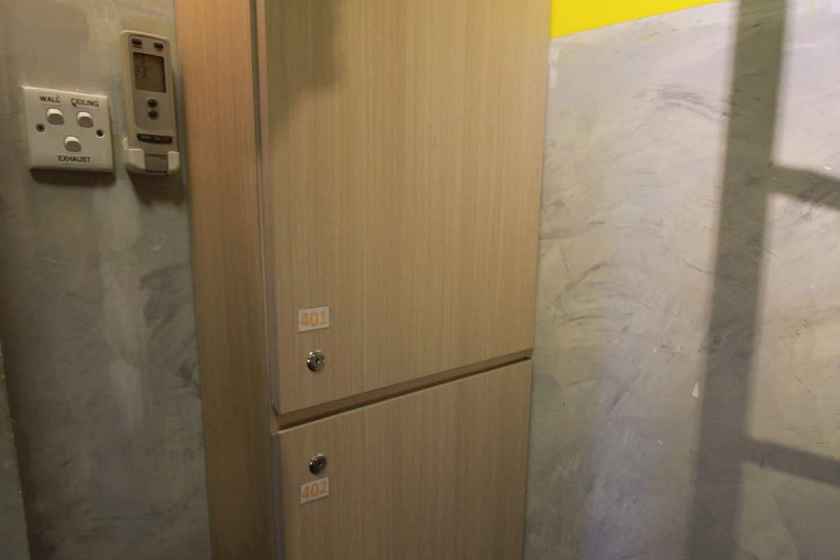 A compact, two-door wooden cabinet with a metallic handle, situated in a room with a yellow and white wall.