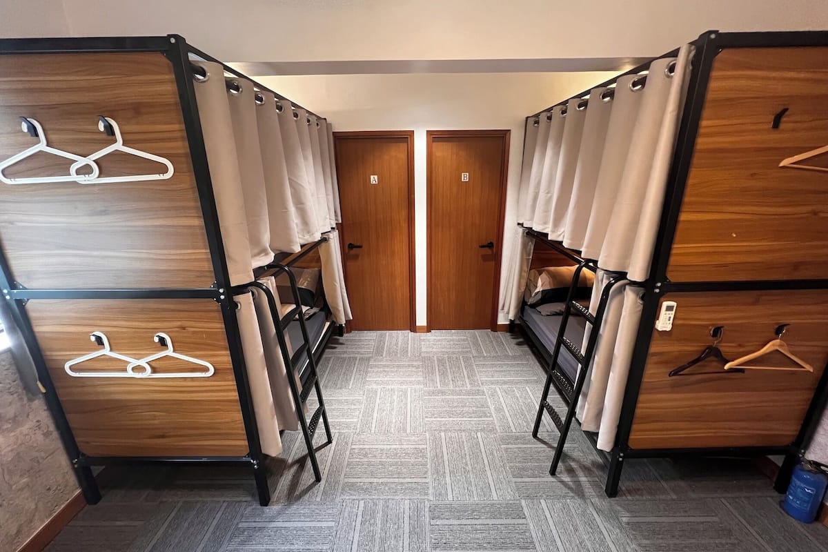A corridor with bunk beds, each with a wooden panel and a hanging clothes rack.