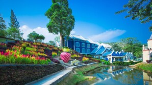 Un jardín ajardinado con un estanque, coloridos parterres de flores y una gran escultura de fresa.