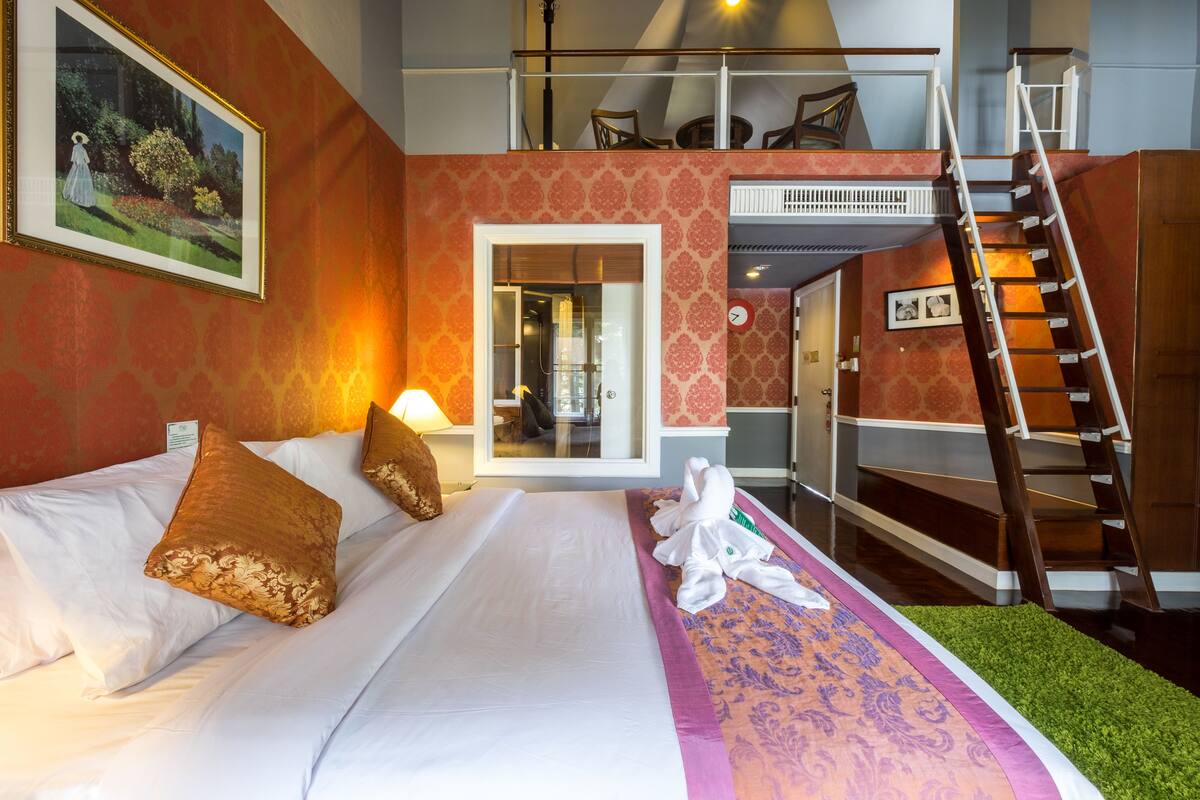 Habitación de hotel con cama, almohadas, alfombra verde, un cuadro, una escalera y una puerta.