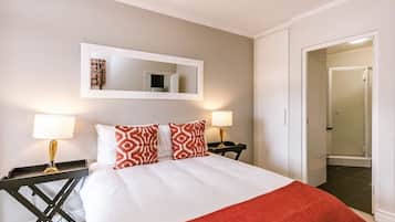 A hotel room with a bed, two bedside lamps, a mirror above the bed, and a door leading to a bathroom.