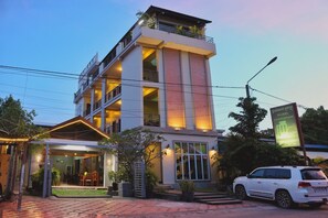 A multi-story building with a covered entrance, a car parked in front, and a signboard. - Neakru Guesthouse and Restaurant (Kampot)