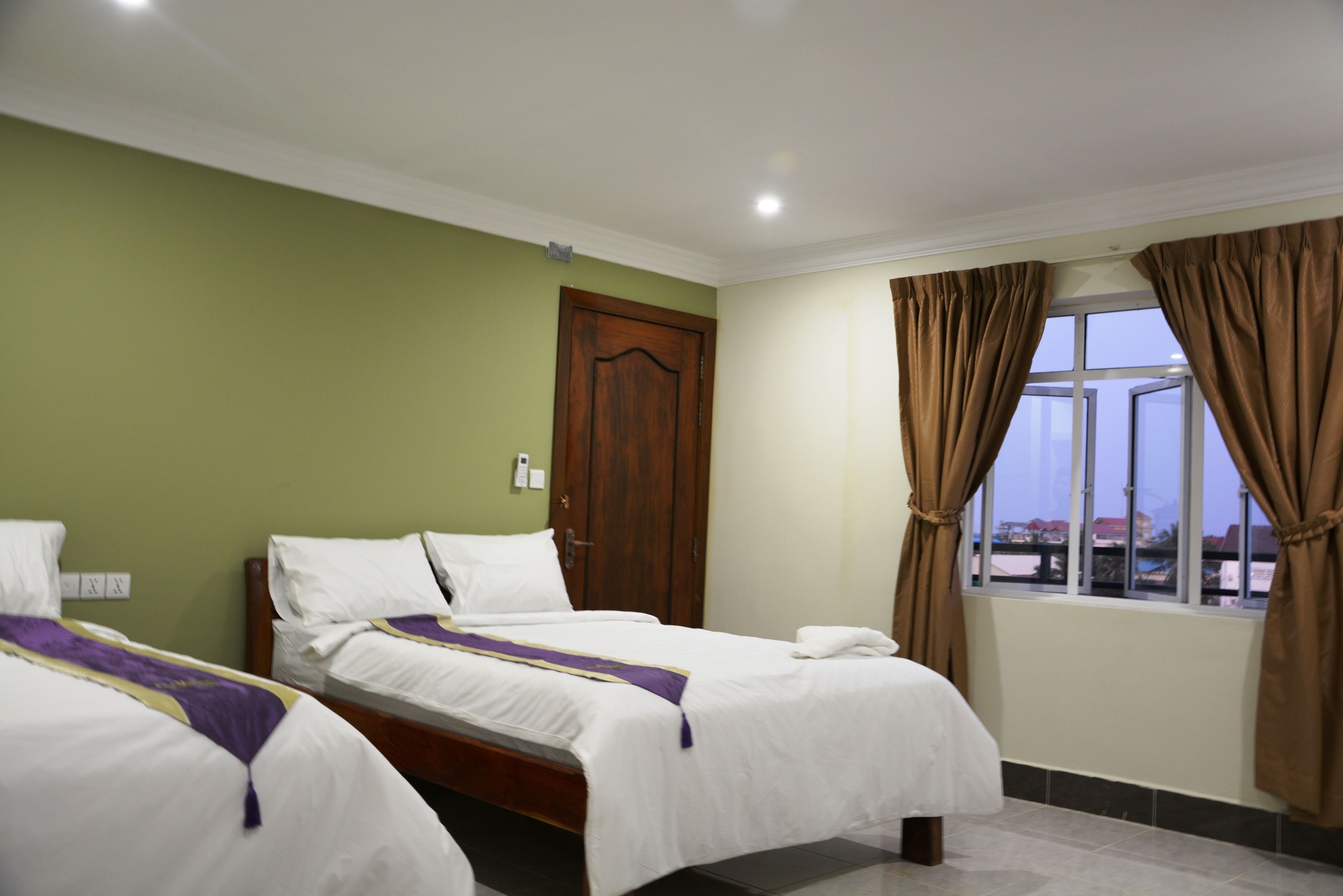 Quarto de hotel com duas camas, uma janela com cortinas e uma porta.