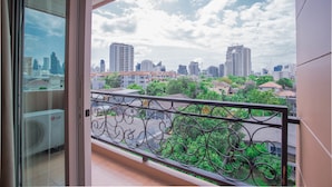 Un balcón con barandilla de hierro forjado que da a una vista panorámica de la ciudad, con edificios altos y zonas verdes.