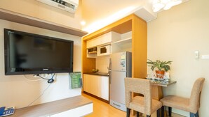 Cocina compacta con refrigerador, microondas y televisor de pantalla plana montado en la pared.