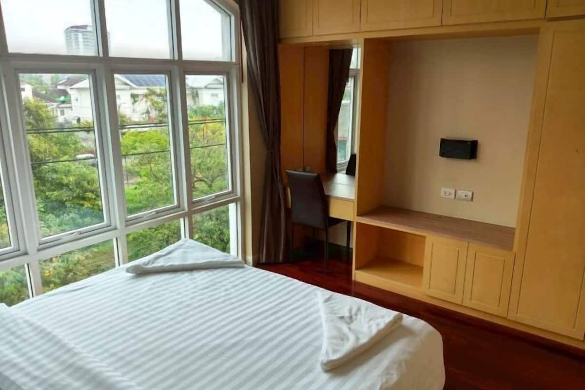 A hotel room with a bed, a desk, a chair, and a view of greenery outside.