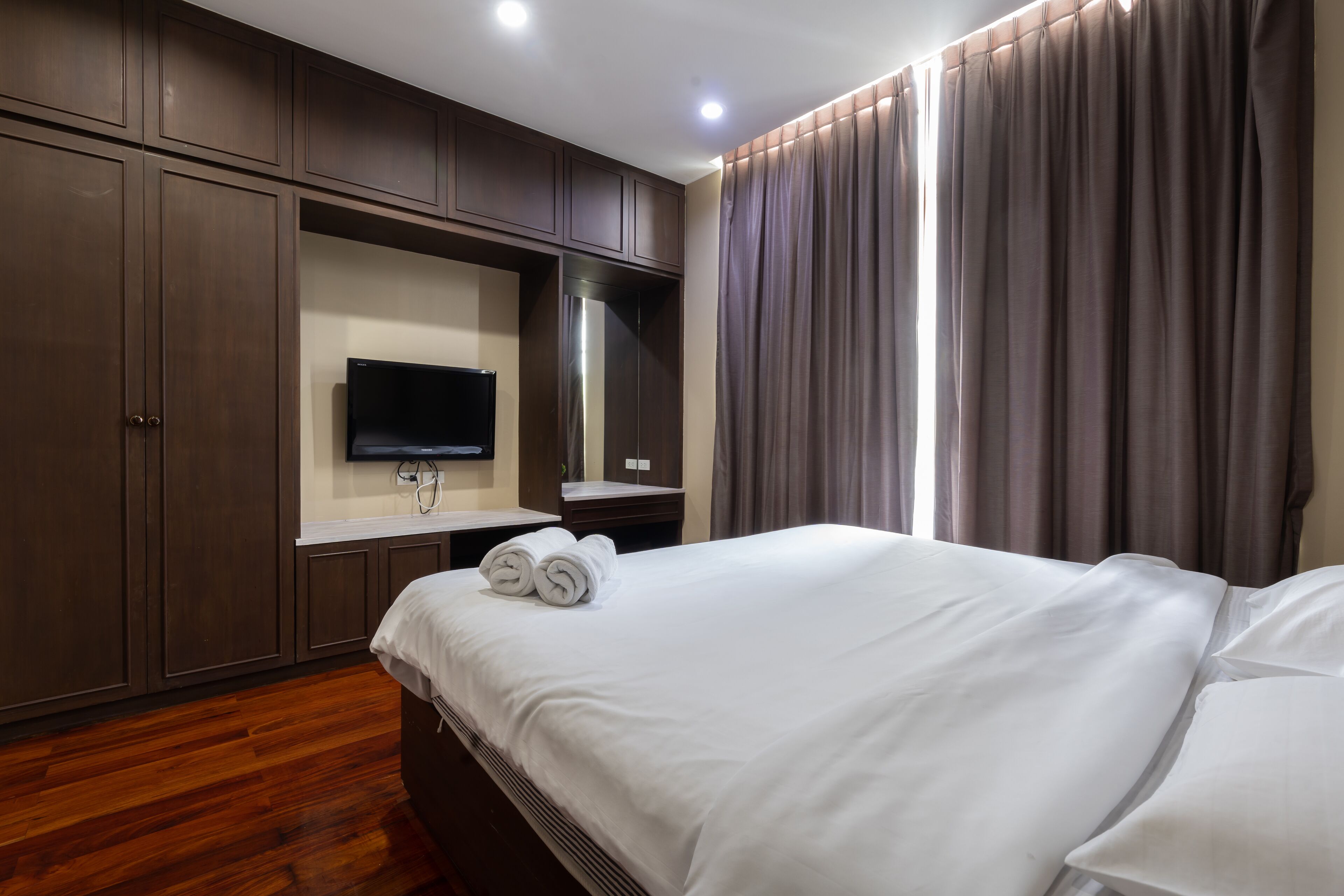 Habitación de hotel con una cama grande, suelo de madera, una televisión de pantalla plana en la pared y un ventanal con cortinas.
