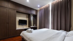 Habitación de hotel con una cama grande, suelo de madera, una televisión de pantalla plana en la pared y un ventanal con cortinas.