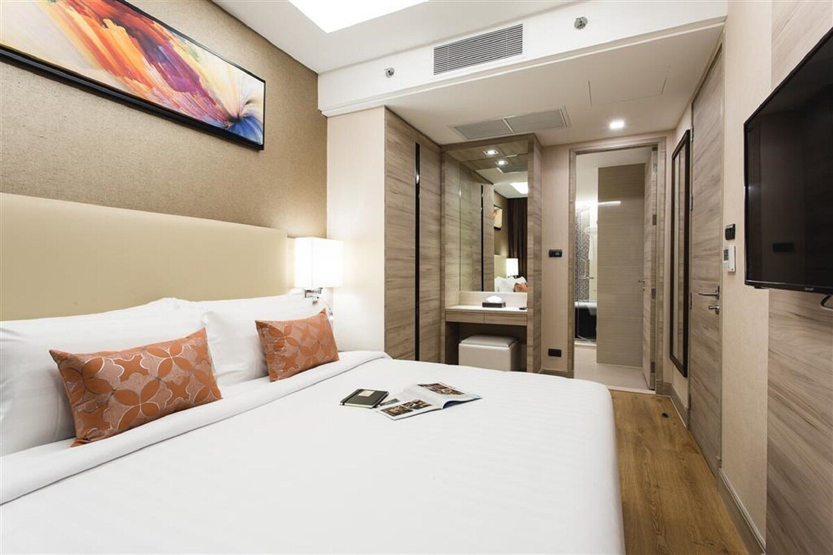 A hotel room with a large bed, a bedside table, a TV, a bathroom with a mirror, and a walk-in closet.