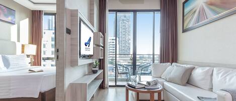 Habitación de hotel moderna con cama, sofá, televisión y balcón con vista a la ciudad.