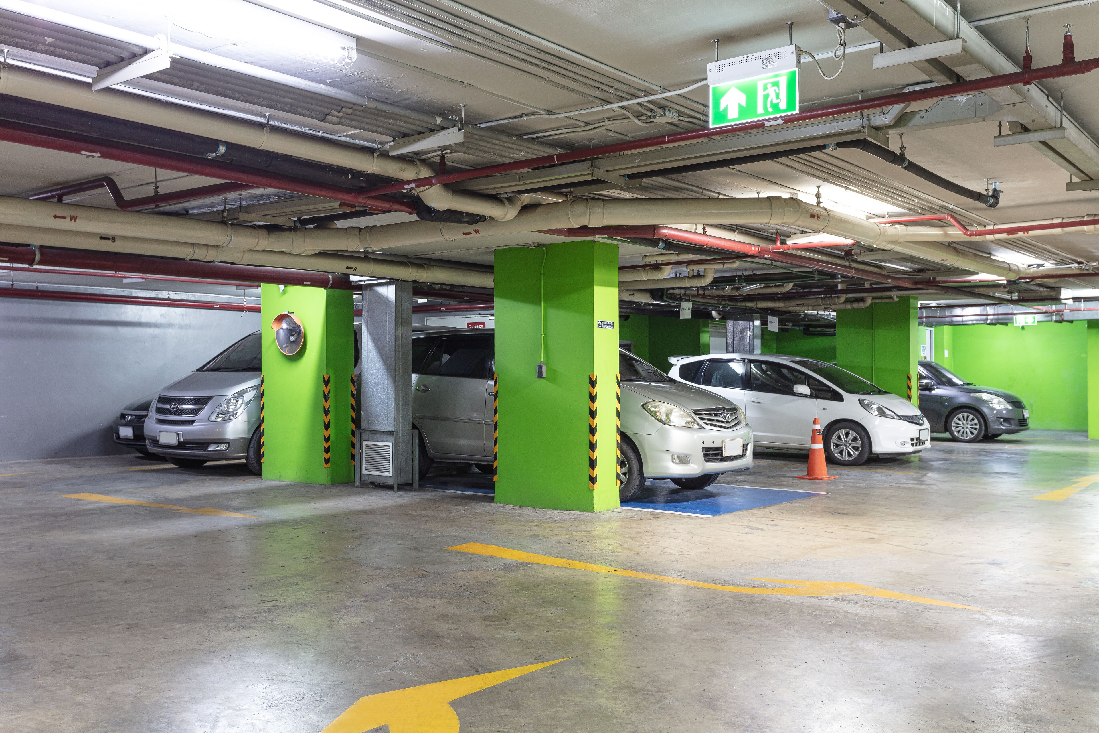 A multi-level parking garage with green pillars, clear directional signage, and a clean, well-maintained floor.