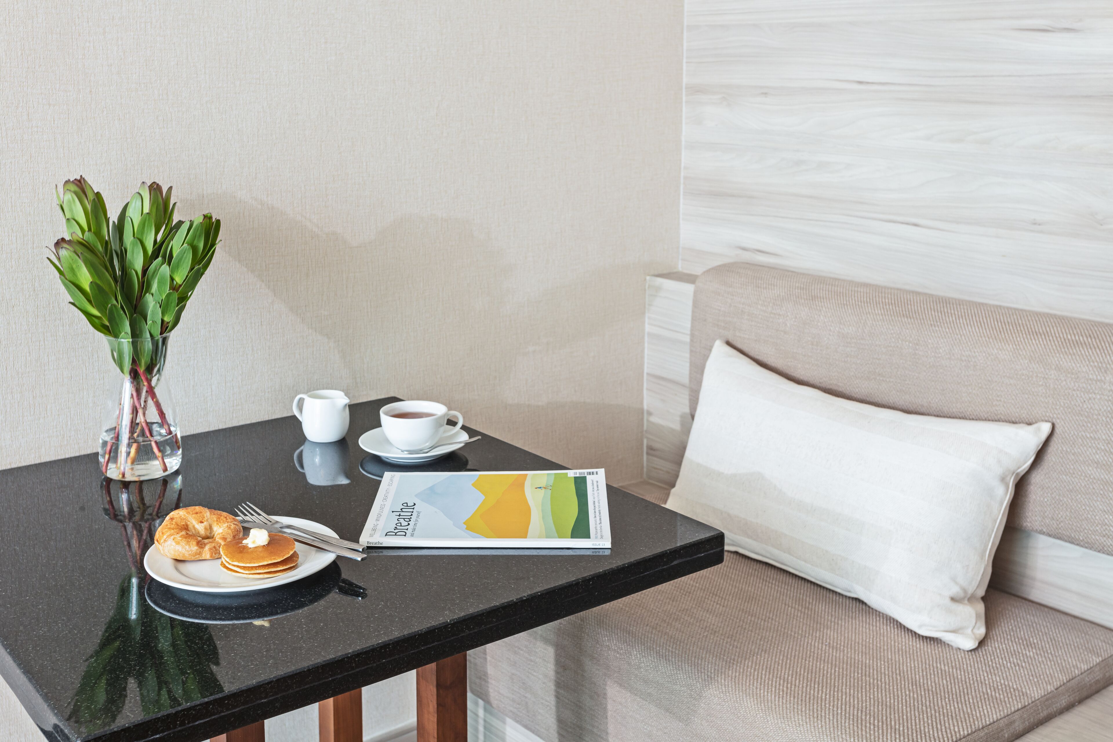 Une table dressée pour le petit-déjeuner avec un croissant, une tasse de café et un magazine.