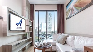 Een moderne hotelkamer met een groot raam, een bank, een bijzettafeltje en een aan de muur bevestigde televisie.