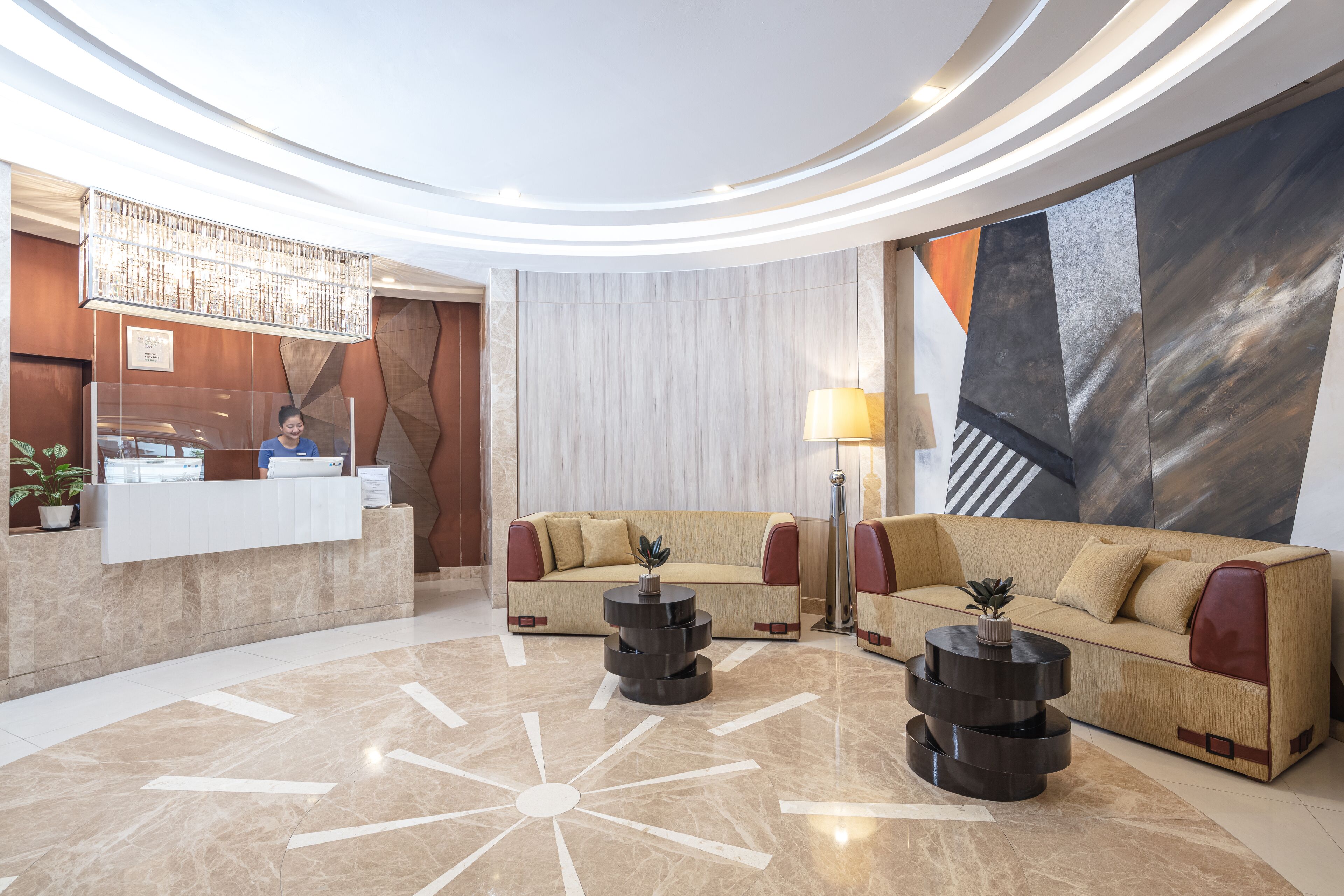 A modern lobby with a reception desk, two sofas, a coffee table, and a large abstract painting on the wall.