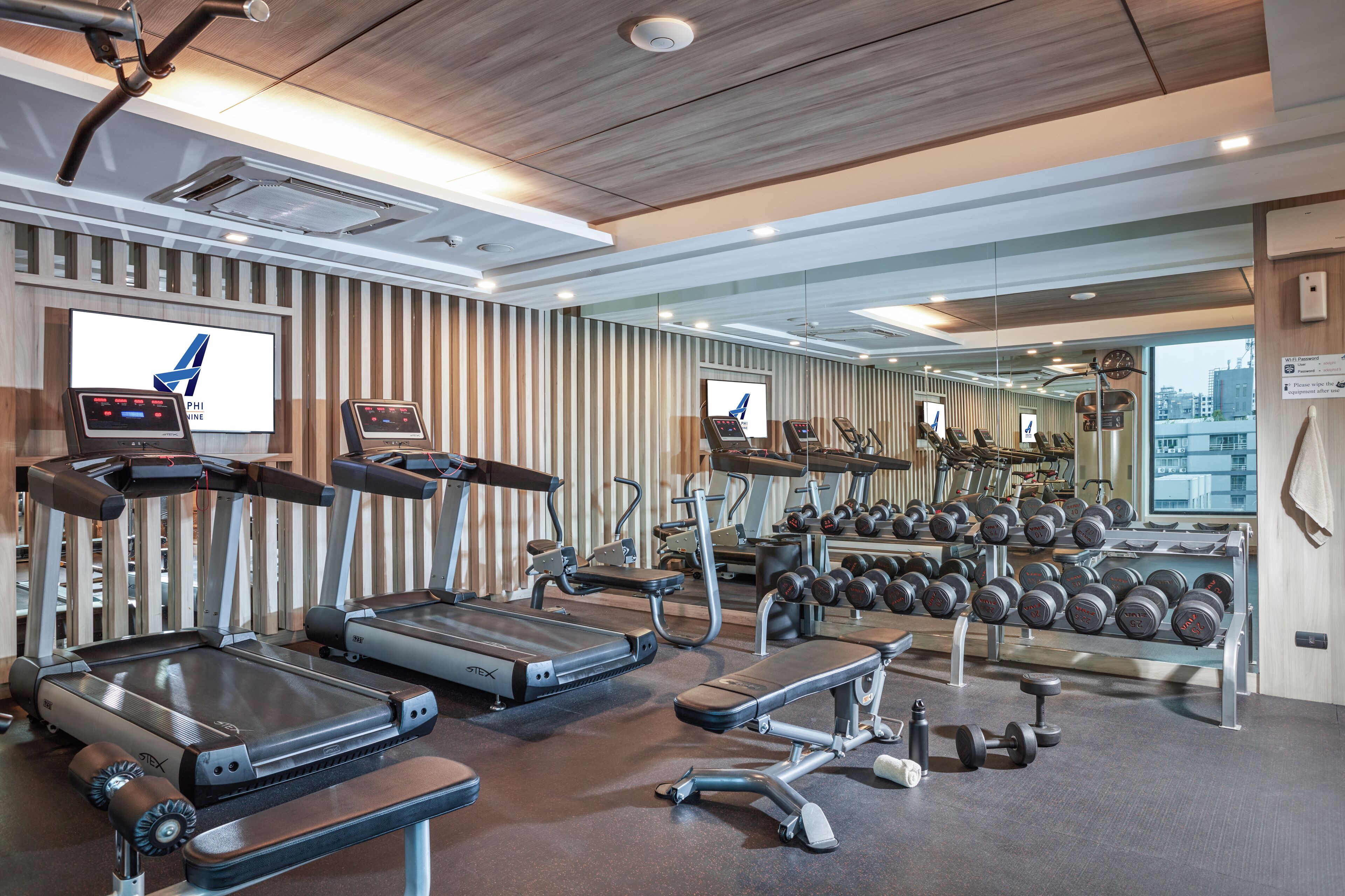 A modern gym with treadmills, weight benches, and dumbbells.