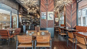 Een modern restaurantinterieur met houten tafels en stoelen, hangende lampen en een bar.