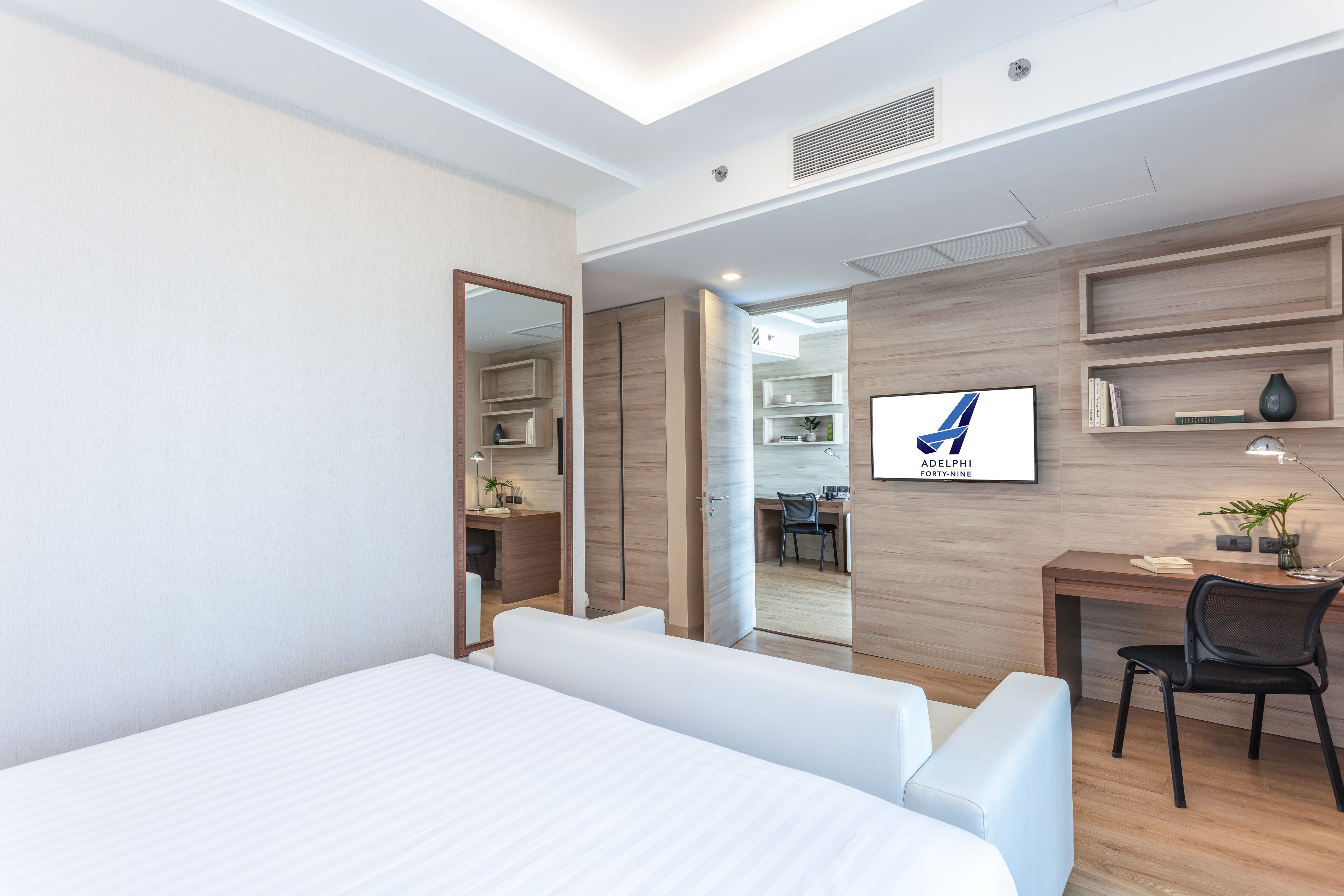 A modern hotel room with a large bed, a desk, a chair, and a TV.