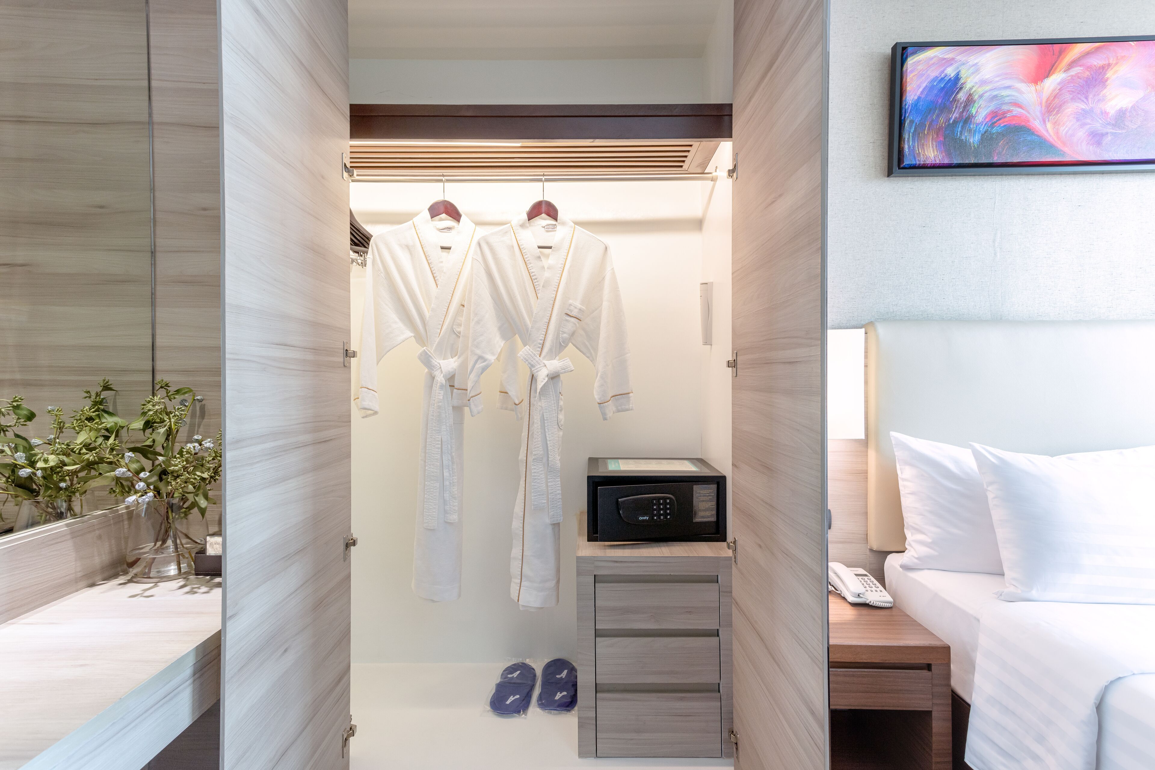 Une chambre d’hôtel dotée d’un dressing contenant deux peignoirs blancs, d’un four à micro-ondes, d’un téléphone sur la table de chevet et d’un petit meuble de rangement.