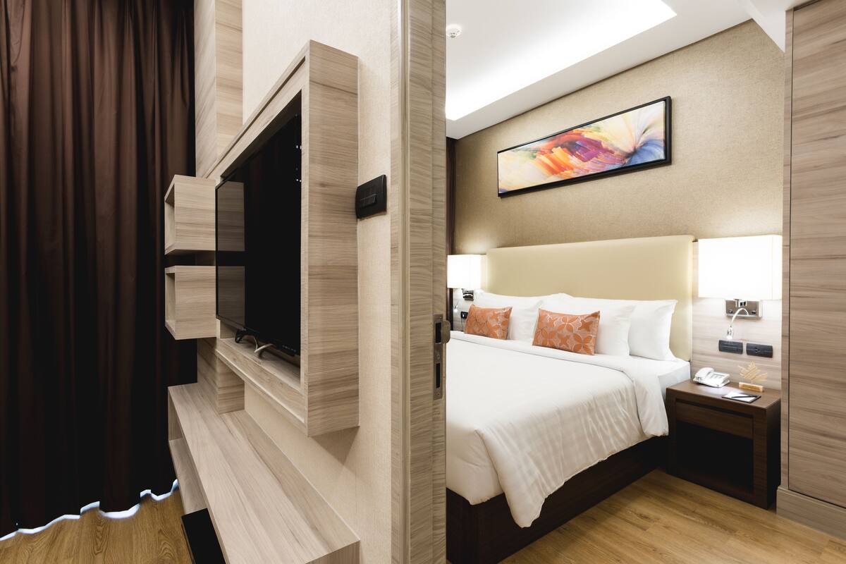 A hotel room with a bed, bedside table, lamp, and a mounted television.