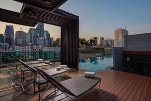 Un salon sur le toit avec des chaises longues, une piscine et une vue panoramique sur la ville.