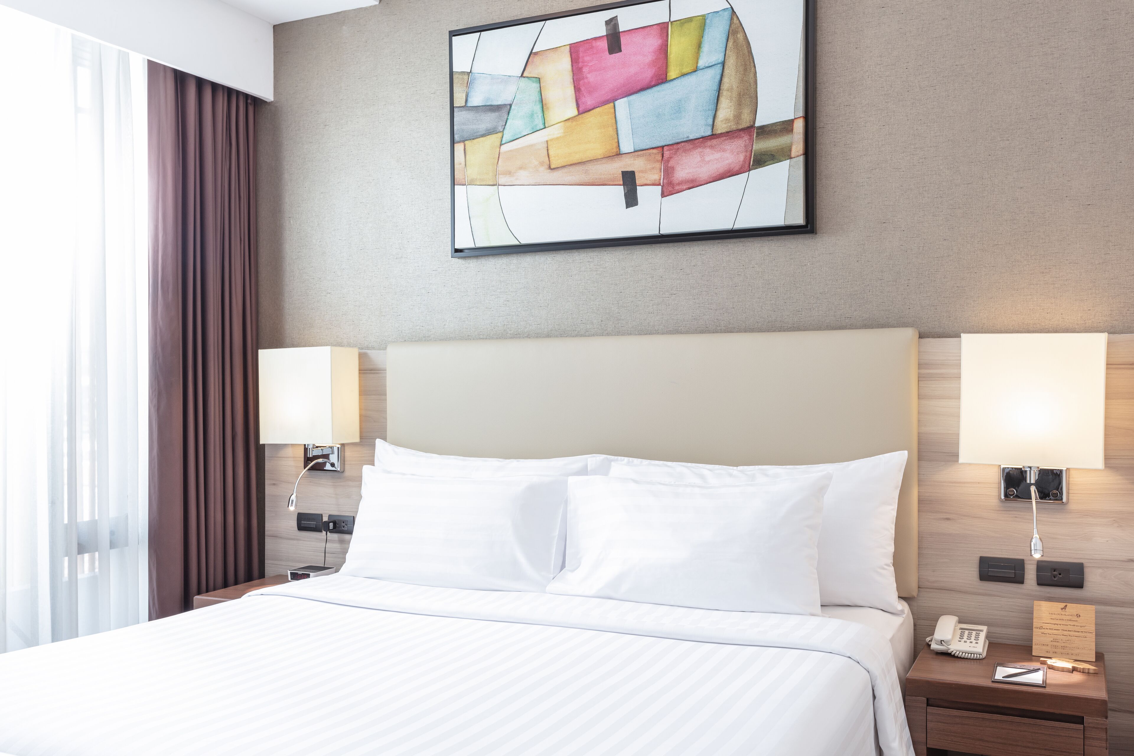 A hotel room with a large bed, two bedside lamps, a phone, and a wall-mounted artwork.