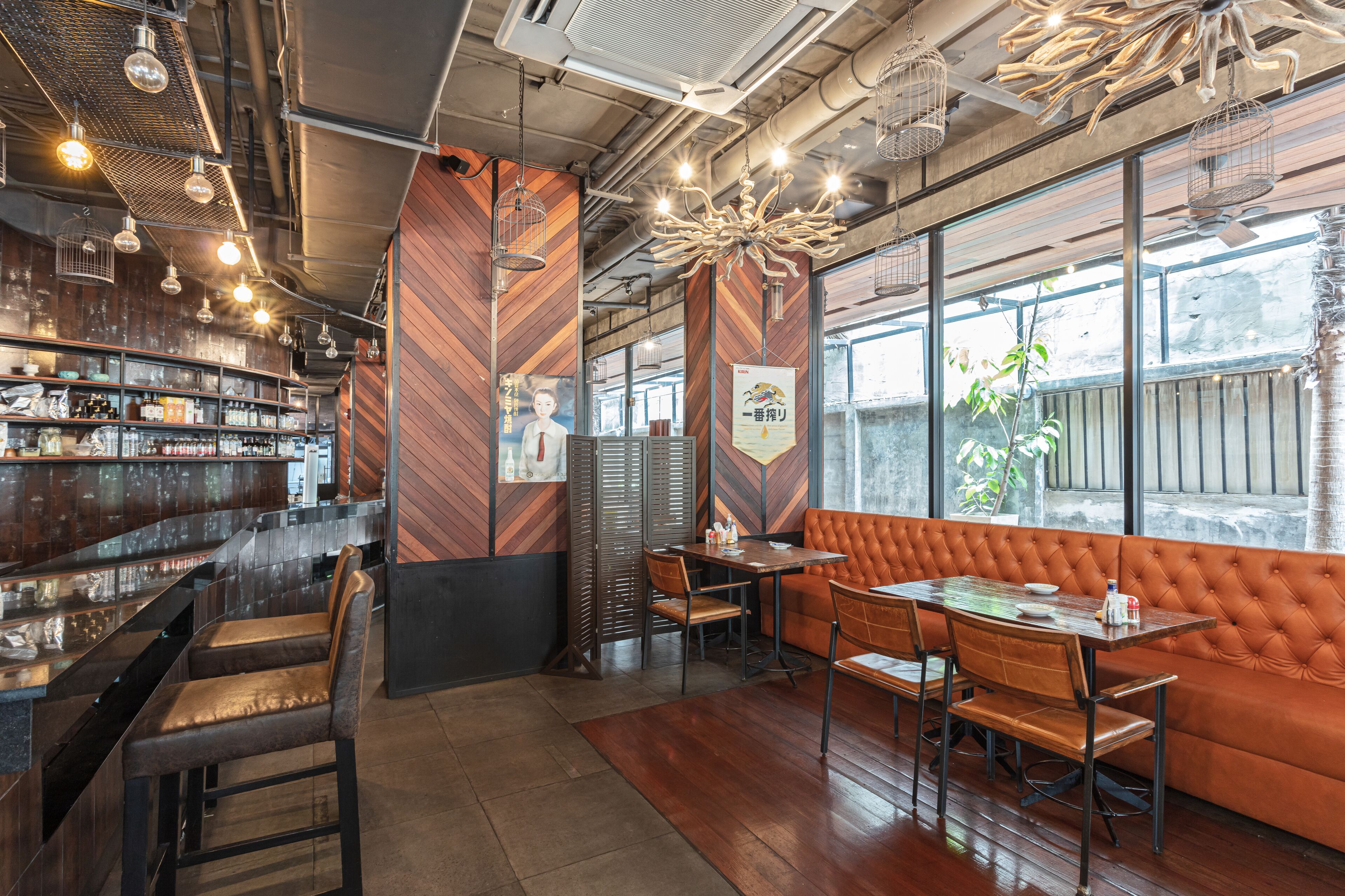 Een restaurantinterieur met een bar, houten wanden en een zithoek met een gestoffeerde bank en tafels.
