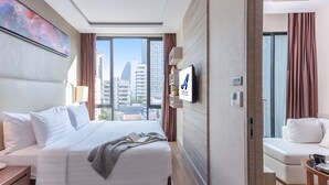 Een moderne hotelkamer met een groot bed, een aan de muur bevestigde televisie, een zithoek met een bank en uitzicht op de stadsbelangrijkste punten door grote ramen.