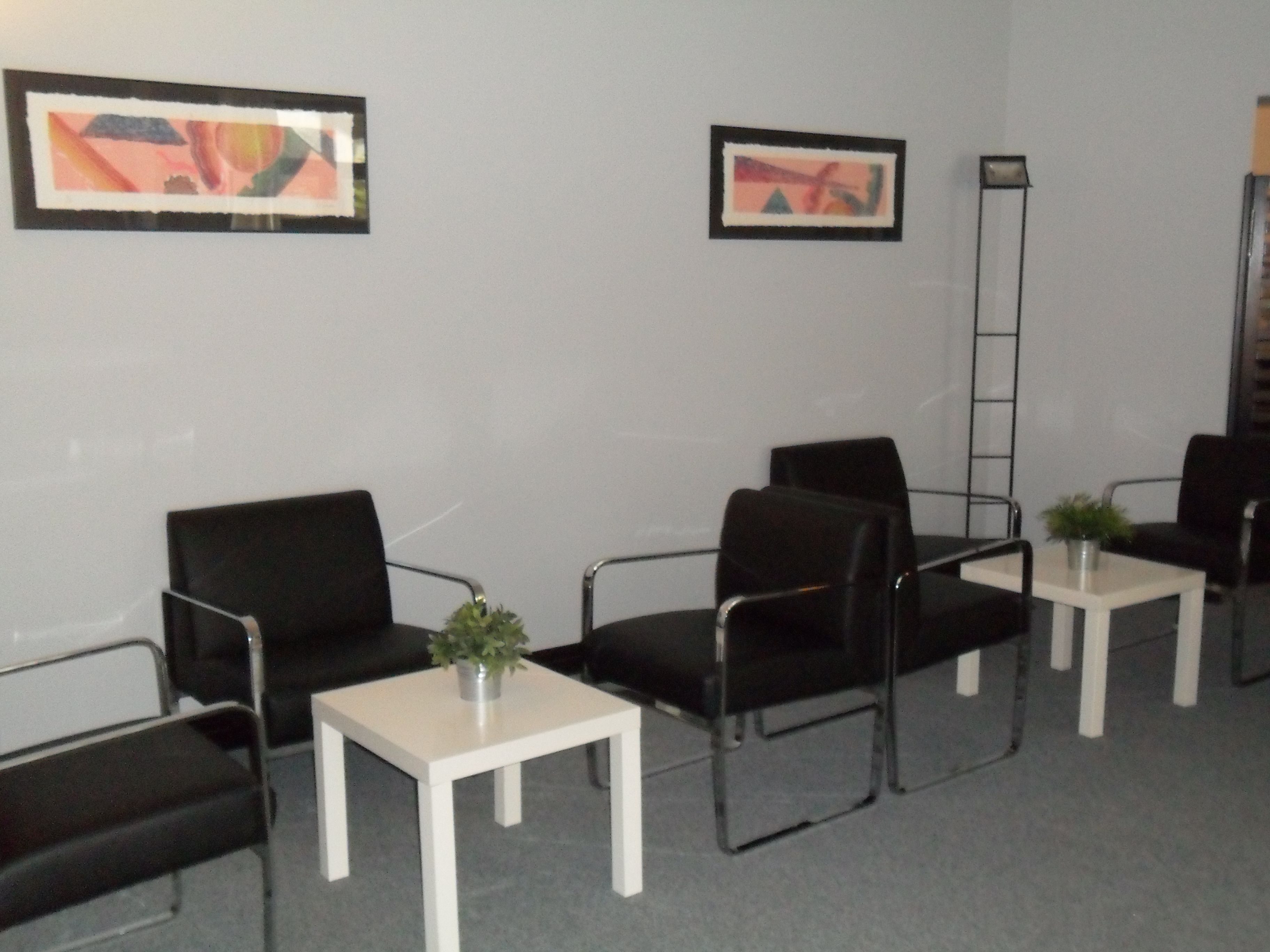 A waiting area with black chairs, white tables, and framed abstract art on the walls.