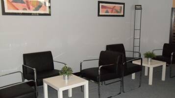 A waiting area with black chairs, white tables, and framed abstract art on the walls.