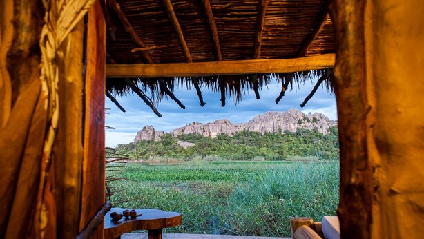 Una estructura de madera con techo de paja que domina un paisaje natural con una montaña al fondo.