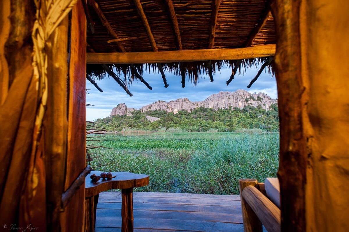 A wooden structure with a thatched roof overlooking a natural landscape with a mountain in the background.