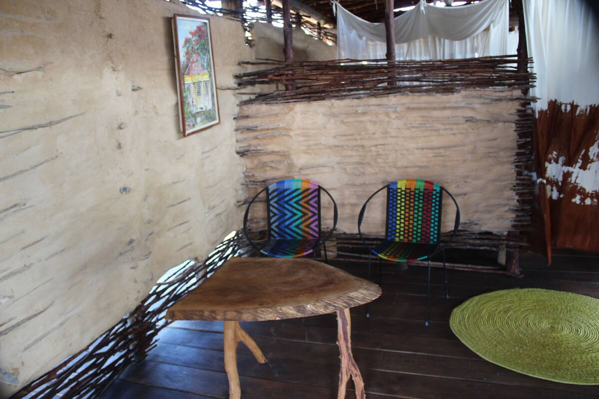 A rustic interior with a woven chair, a wooden table, and a woven mat on the floor.